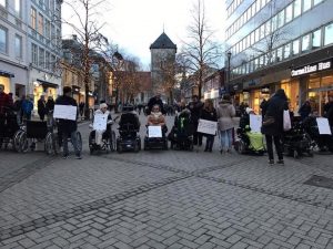 Mange personer med plakater, de fleste i rullestol, sperrer av en gågate